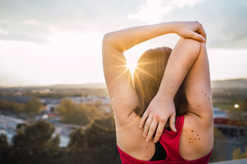Caucasian woman stretching triceps and warming up to run in front of the sunset. Workout and exercise concept. Healthy in nature concept.
