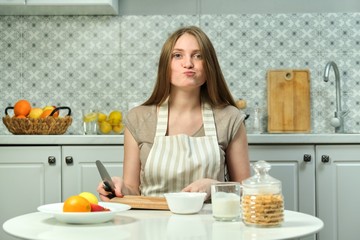 Young woman sitting in kitchen with fruit products knife cutting board