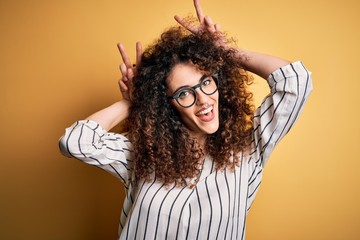 Young beautiful woman with curly hair and piercing wearing striped shirt and glasses Posing funny...
