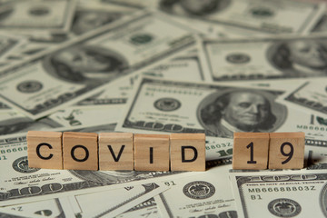 COVID-19 coronavirus with wooden alphabet blocks, on 100 dollar money background with copy space.