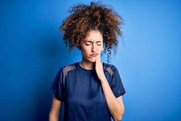 Fototapeta na wymiar Young beautiful woman with curly hair and piercing wearing casual blue t-shirt touching mouth with hand with painful expression because of toothache or dental illness on teeth. Dentist