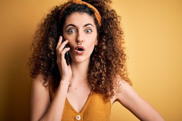 Young beautiful woman with curly hair and piercing having conversation talking on smartphone scared in shock with a surprise face, afraid and excited with fear expression