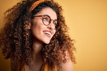 Beautiful brunette woman on vacation with curly hair and piercing wearing glasses and diadem looking away to side with smile on face, natural expression. Laughing confident.