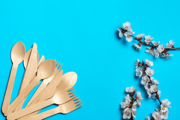 Disposable wooden forks and spoons are fan-shaped in the corner. blue background and several twigs of flowering trees