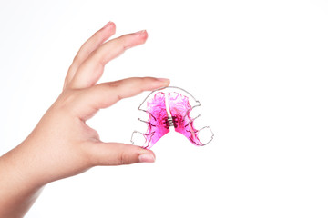 A girl's hand holds her pink orthodontic appliance on a white background. Concept of oral health in childhood. Space for text.