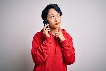 Young beautiful asian girl having conversation talking on the smartphone over white background...