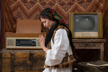 Waist up photo of a young woman in national white dress and black handkerchief who praying with closed eyes