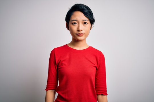 Young beautiful asian girl wearing casual red t-shirt standing over isolated white background Relaxed with serious expression on face. Simple and natural looking at the camera.