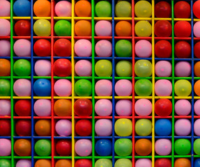 Wall of small coloured balloons at a carnival. The balloons are orange, pink, blue, red, green and yellow. The display is used as part of a throwing darts game of chance at an arcade. 