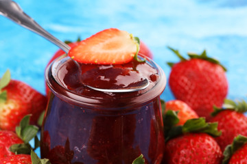 Strawberry jam in a glass jar with strawberries and leaves on rustic background. Homemade strawberry marmelade or jam