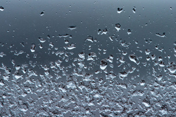 Freezing rain on a pane of clear glass. The ice particles are attached to the glass with the cold temperatures. The top droplets are more liquid and the lower portions are solid and have crystallized.