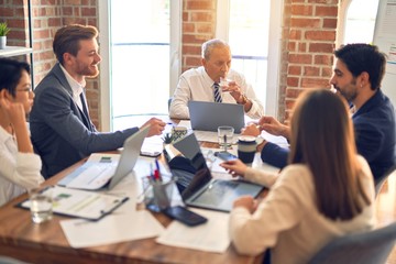 Group of business workers working together. Sitting on desk using laptop and talking at the office