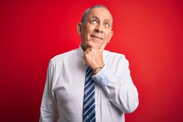 Senior handsome businessman wearing elegant tie standing over isolated red background with hand on chin thinking about question, pensive expression. Smiling with thoughtful face. Doubt concept.