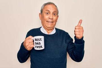 Senior man drinking cup of coffee with best dad ever message over white background happy with big smile doing ok sign, thumb up with fingers, excellent sign