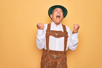 Senior grey-haired man wearing german traditional octoberfest suit over yellow background crazy and...