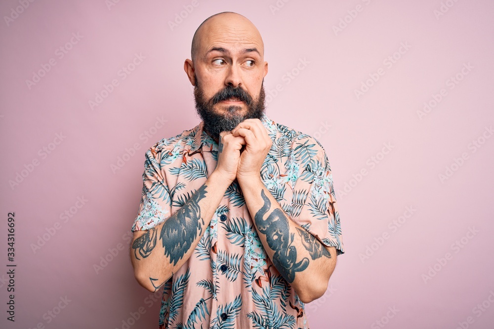 Sticker handsome bald man with beard and tattoo wearing casual floral shirt over pink background laughing ne