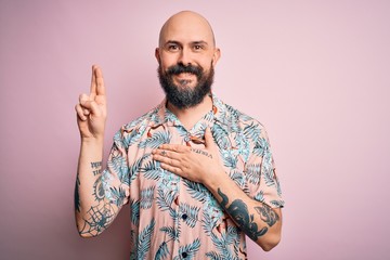 Handsome bald man with beard and tattoo wearing casual floral shirt over pink background smiling...