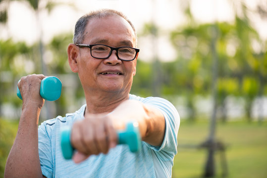 Asian Old Man Doing Physical Exercise Outdoor With Dumbbells. Be Healthy And Strong, Work On The Muscles. Senior Healthcare And Sport Concept.