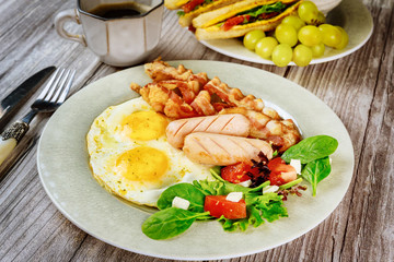 Traditional English breakfast with bacon, eggs, sausages, salad and grilled cheese toast.