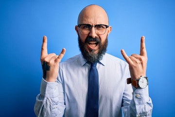 Handsome business bald man with beard wearing elegant tie and glasses over blue background shouting...
