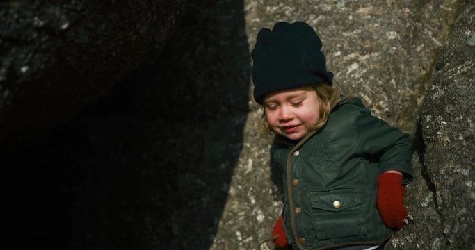 Little preschooler standing by rocks in winter time