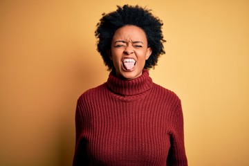 Fototapeta na wymiar Young beautiful African American afro woman with curly hair wearing casual turtleneck sweater sticking tongue out happy with funny expression. Emotion concept.