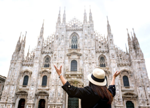 Duomo di Milano, back female tourist raising hands up in front of Cathedral im Milan, Italy