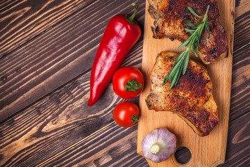 Grilled pork steaks and vegetables on a rustic wooden table. Grilled meat on the bone with spices, garlic, peppers, tomatoes and rosemary. Restaurant menu. view from above