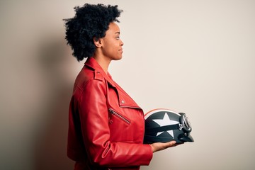Young African American afro motorcyclist woman with curly hair holding motorcycle helmet looking to...