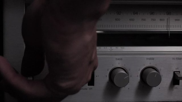 Slow motion hand reaching in to turn on power switch for old school AM FM wireless radio player. Orange light on system light up with various switches in macro shot.