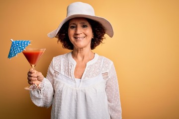 Middle age curly hair woman on holiday drinking cocktail over isolated yellow background with a happy face standing and smiling with a confident smile showing teeth