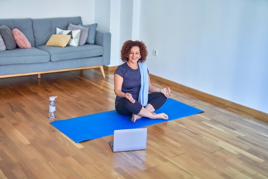 Middle age beautiful sportswoman smilig happy. Sitting on mat with smile on face using laptop at home