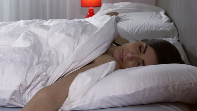 Young woman in bed waking up in hte morning in white bed