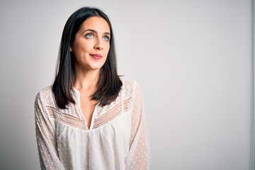 Fototapeta premium Young brunette woman with blue eyes wearing casual t-shirt over isolated white background smiling looking to the side and staring away thinking.
