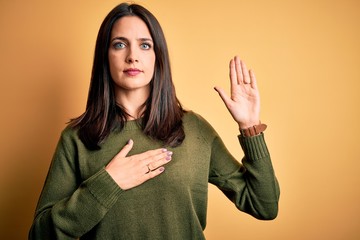Young brunette woman with blue eyes wearing green casual sweater over yellow background Swearing...