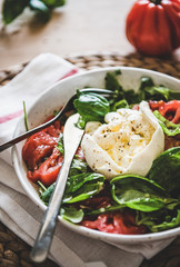 Traditional Italian salad with Buratta cheese, tomatoes, arugula and fresh basil in white bowl over wooden table background, selective focus, close-up. Classical Italian cuisine concept