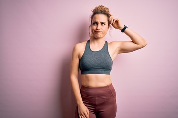 Young beautiful blonde sportswoman doing sport wearing sportswear over pink background confuse and...