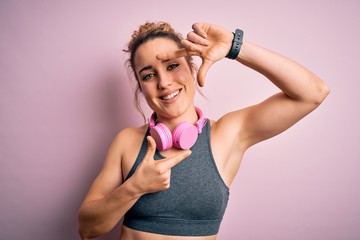 Young beautiful blonde sportswoman wearing sportswear listening to music using headphones smiling making frame with hands and fingers with happy face. Creativity and photography concept.