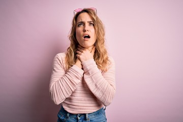 Young beautiful blonde woman wearing casual sweater and sunglasses over pink background shouting and suffocate because painful strangle. Health problem. Asphyxiate and suicide concept.