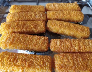 Cod sticks, breaded, close up. Cooked fish fingers baked in a glass oven-tray.