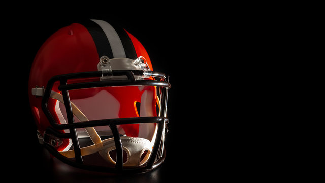 Dark side of college sports concept with high contrast lighting on american football helmet illuminated by dramatic hard light with harsh shadows isolated on black background with copy space