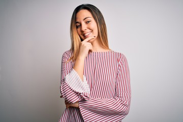 Young beautiful blonde woman with blue eyes wearing stiped t-shirt over white background looking...