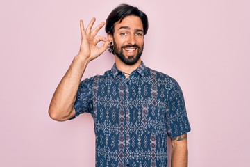 Fototapeta premium Young handsome hispanic bohemian man wearing hippie style over pink background smiling positive doing ok sign with hand and fingers. Successful expression.