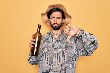 Young handsome hispanic bohemian hipster man with bear drinking from a empty wine bottle with angry...