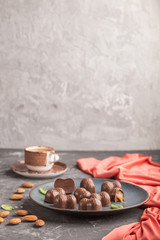 Chocolate caramel candies with almonds and a cup of coffee on a black concrete background. side view, copy space.