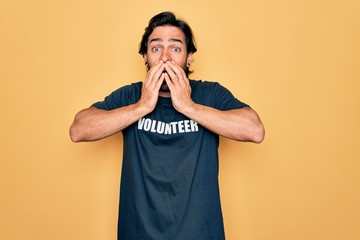 Young handsome hispanic volunteer man wearing volunteering t-shirt as social care laughing and embarrassed giggle covering mouth with hands, gossip and scandal concept