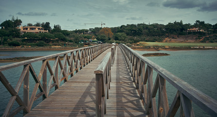Fototapeta premium Quinta do Lago view in Algarve, Portugal. Wooden bridge along the river and blue sky with clouds