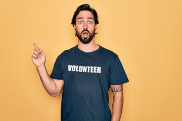 Young handsome hispanic volunteer man wearing volunteering t-shirt as social care Surprised...