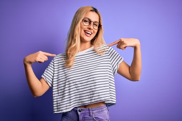 Young beautiful blonde woman wearing striped t-shirt and glasses over purple background looking confident with smile on face, pointing oneself with fingers proud and happy.