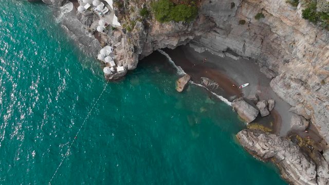 Aerial drone view pull back revealing shot of remote hidden sandy beach swimming people in sea bay with transparent blue water in summer. Amalfi coast Italy